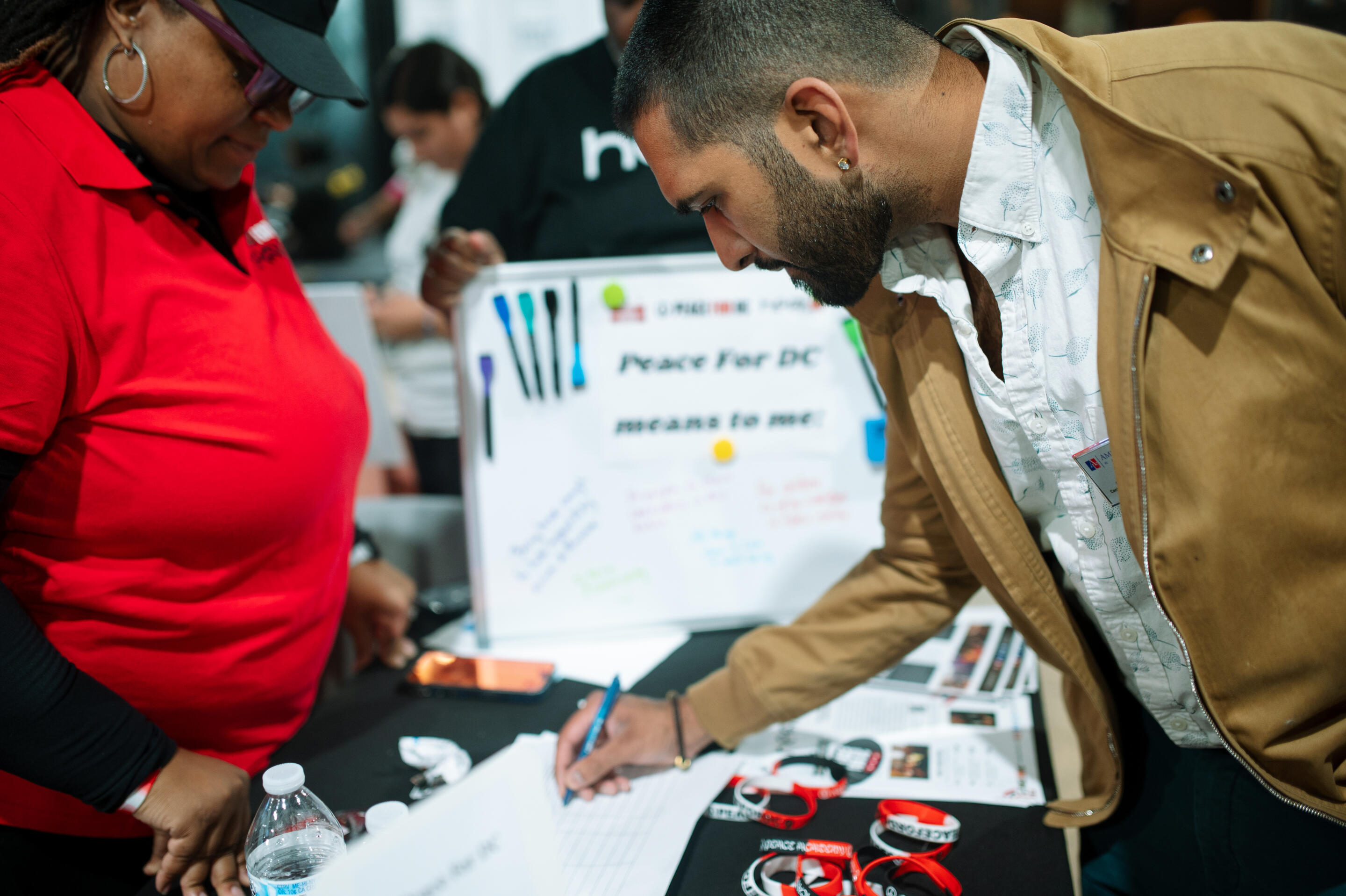 Photo at Spur Local's Community Changemakers 2025 event, showing an event attendee wearing a tan jacket signing a piece of paper at a nonprofit table. Photo courtesy of Fleur Louise Photography