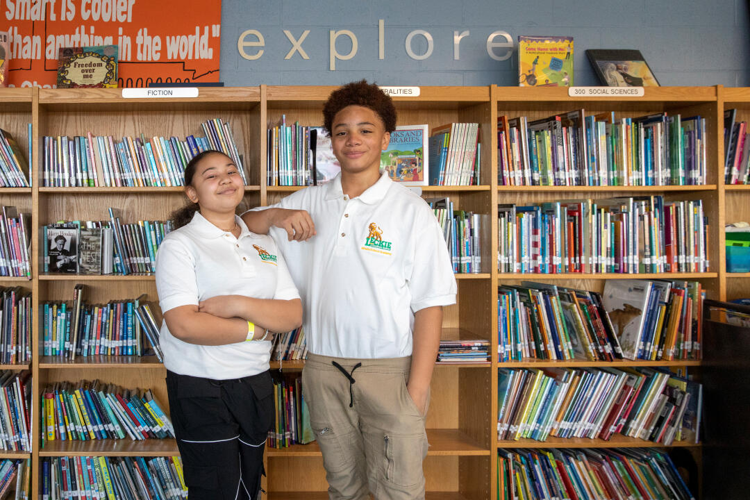 Photo of two young students smiling at the camera with shelves of books behind them, courtesy of After-School All-Stars DC