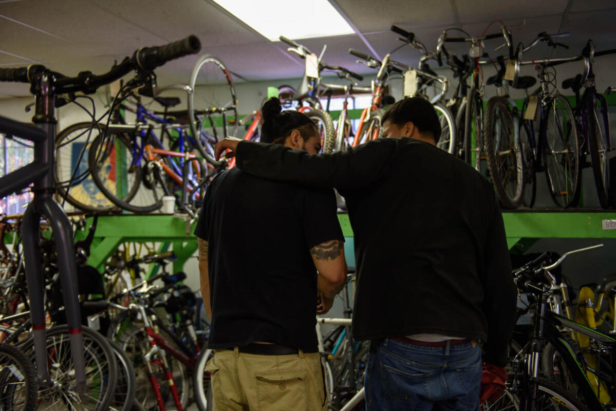 Photo of two adults standing in a bike shop, with one putting their arm around the other's shoulders